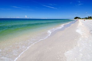A beach with clear water, a sandy shore, and a distant tree line. - Beachfront Community w/ Pool, Workout Room + Tennis - Mansions By the Sea 406B (TREASURE ISLAND)