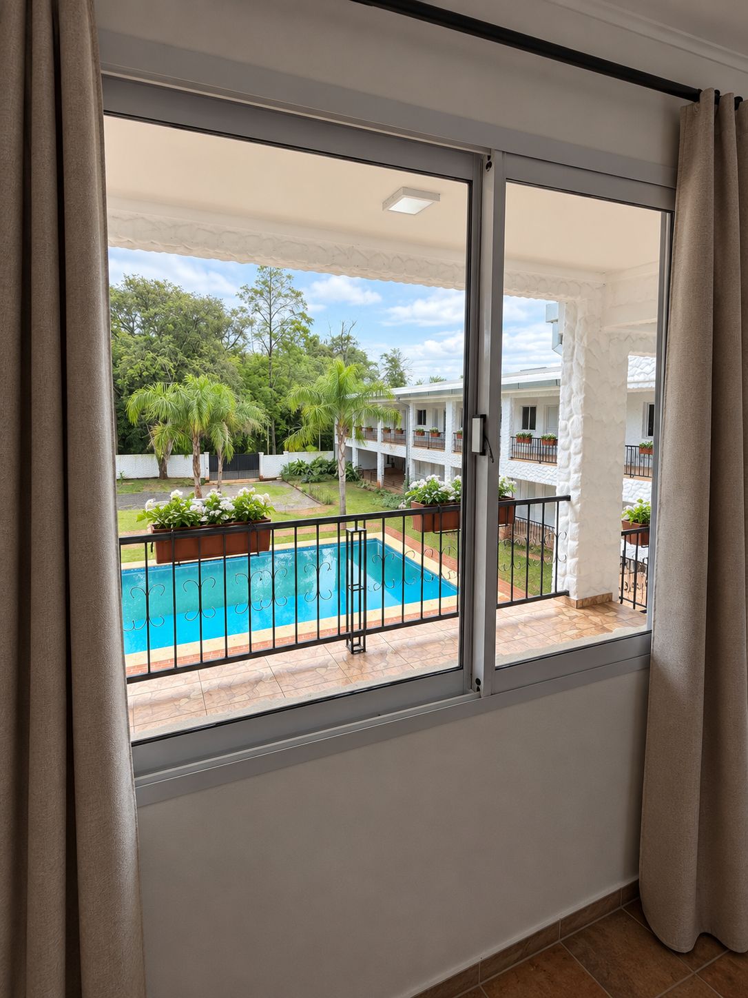 A balcony with a view of a swimming pool, greenery, and a building with balconies.