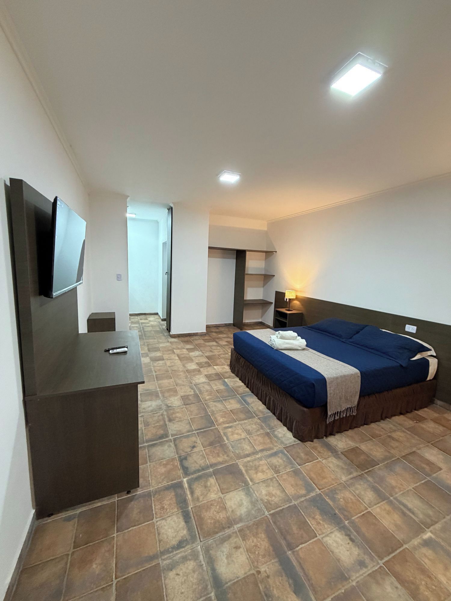 Quarto de hotel com cama, escrivaninha, televisão e banheiro.