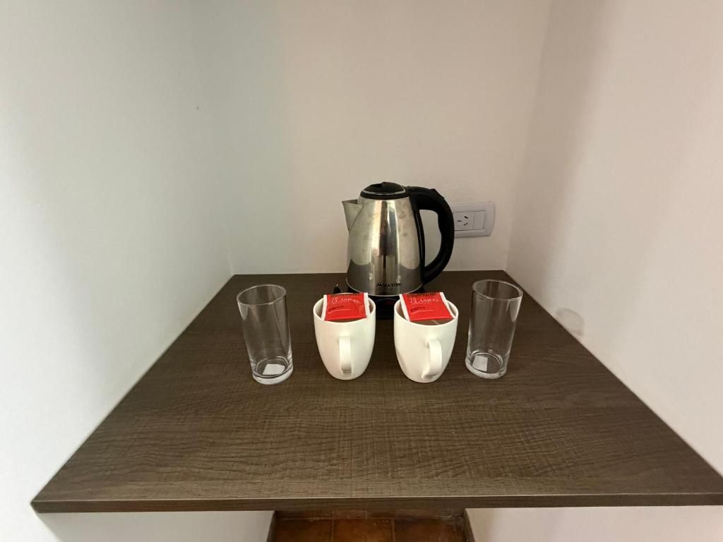 Uma mesa com uma chaleira e quatro chávenas, duas com saquinhos de chá.