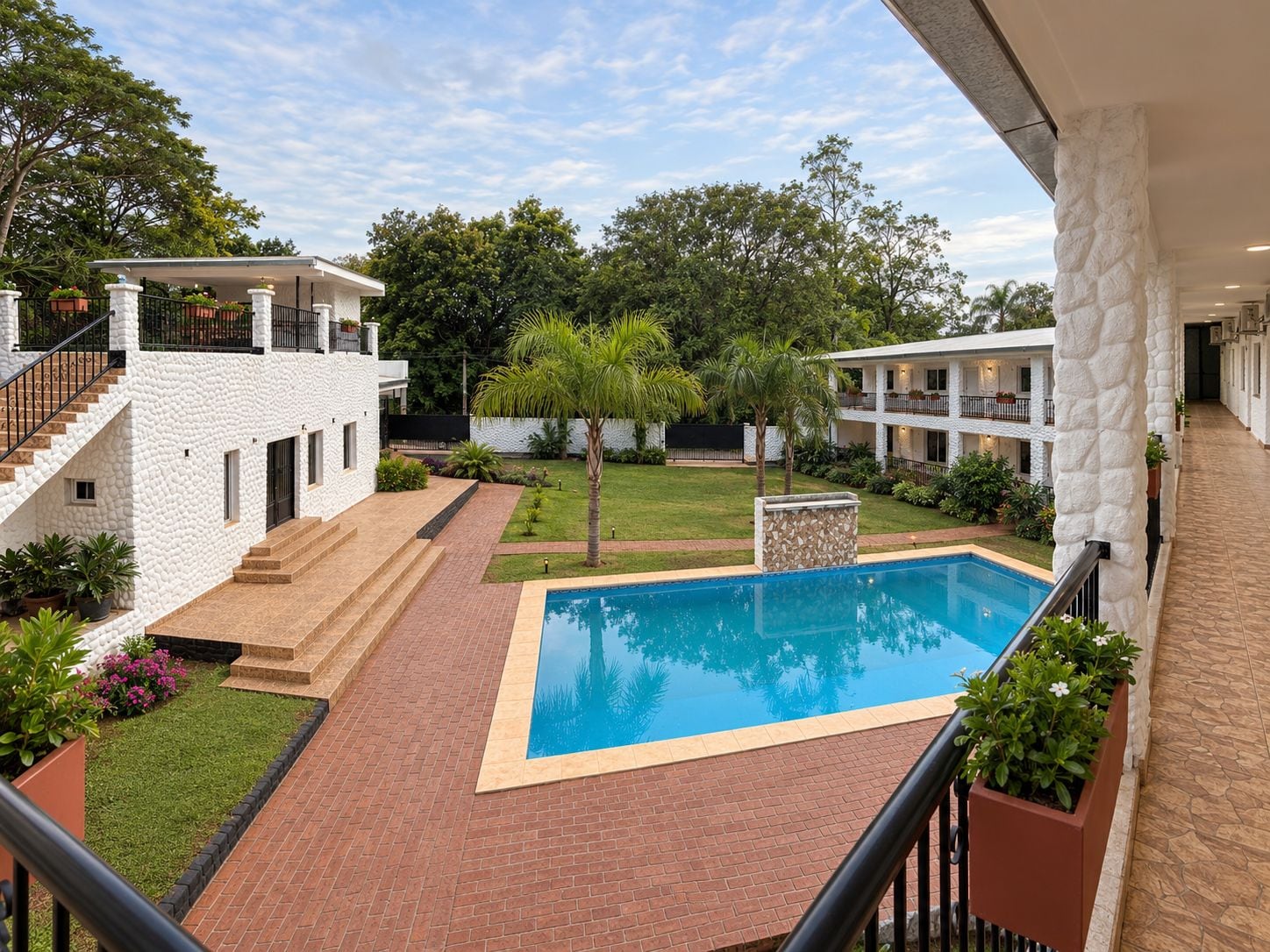 A pool area with a clear blue pool, surrounded by a brick patio, and adjacent to a white building with a balcony.