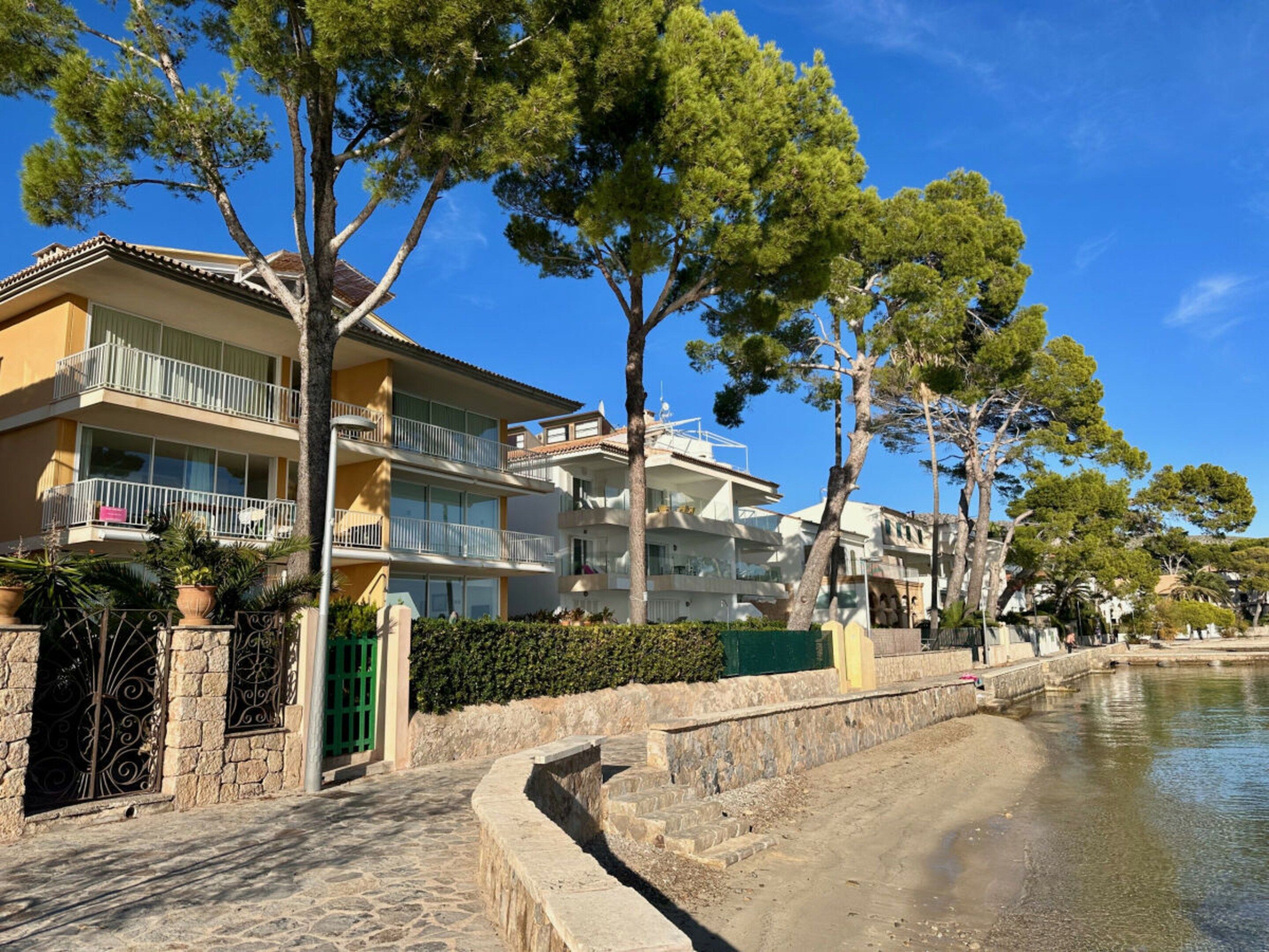 A coastal building with balconies, a stone pathway, and a body of water.