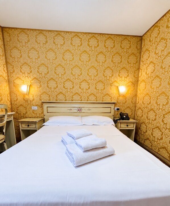 Une chambre d’hôtel avec un grand lit, deux tables de chevet, une petite table et un téléphone fixé au mur.