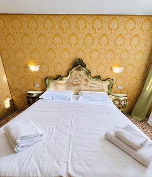 Une chambre d’hôtel avec un grand lit, deux tables de chevet et une tête de lit ornée d’un motif décoratif.