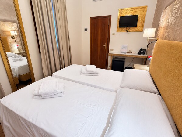 Habitació d'hotel amb dos llits, una taula de treball, un televisor i un mirall.