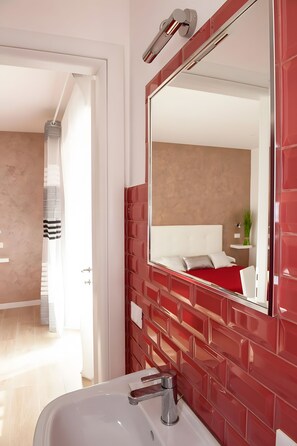 A modern bathroom with a red-tiled wall, a white sink, and a large mirror. - Apartment 'Doppia Con Balcone' with Balcony, Wi-Fi and Air Conditioning (Roma)