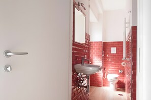 A bathroom with a red brick wall, a white sink, and a toilet. - Apartment 'Doppia Con Balcone' with Balcony, Wi-Fi and Air Conditioning (Roma)
