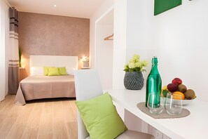 Ein modernes Hotelzimmer mit einem Bett, einem Schreibtisch mit Blumen in einer Vase, einer Flasche und einer Schale mit Obst.
