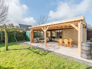 A covered patio with a wooden pergola, outdoor seating, and a barrel. - Holiday Home in Renesse With Swimming Pool (Renesse)
