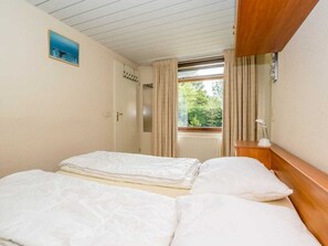 A room with two beds, a window with curtains, a wooden headboard, and a small painting on the wall. - Holiday Home in Renesse With Swimming Pool (Renesse)