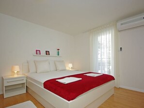 Ein modernes Schlafzimmer mit einem großen Bett, Nachttischen, einer roten Tagesdecke und einem Fenster mit Vorhängen.
