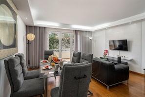 A modern living room with a glass table, grey sofas, a flat-screen TV, and a balcony with curtains. - Apartment in Caniço near facilities|Boeiro Living (Caniço)
