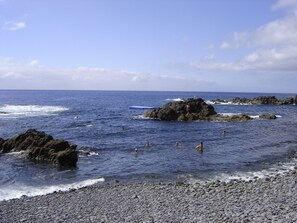 A rocky shoreline with clear blue water and a few people swimming. - Apartment in Caniço near facilities|Boeiro Living (Caniço)