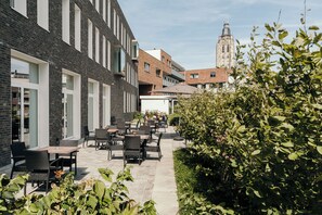 An outdoor patio area with tables and chairs, surrounded by greenery and a brick building. - Spacious Deluxe Studio with Full Kitchen, Nespresso & Comfortable Living Space (Oudenaarde)