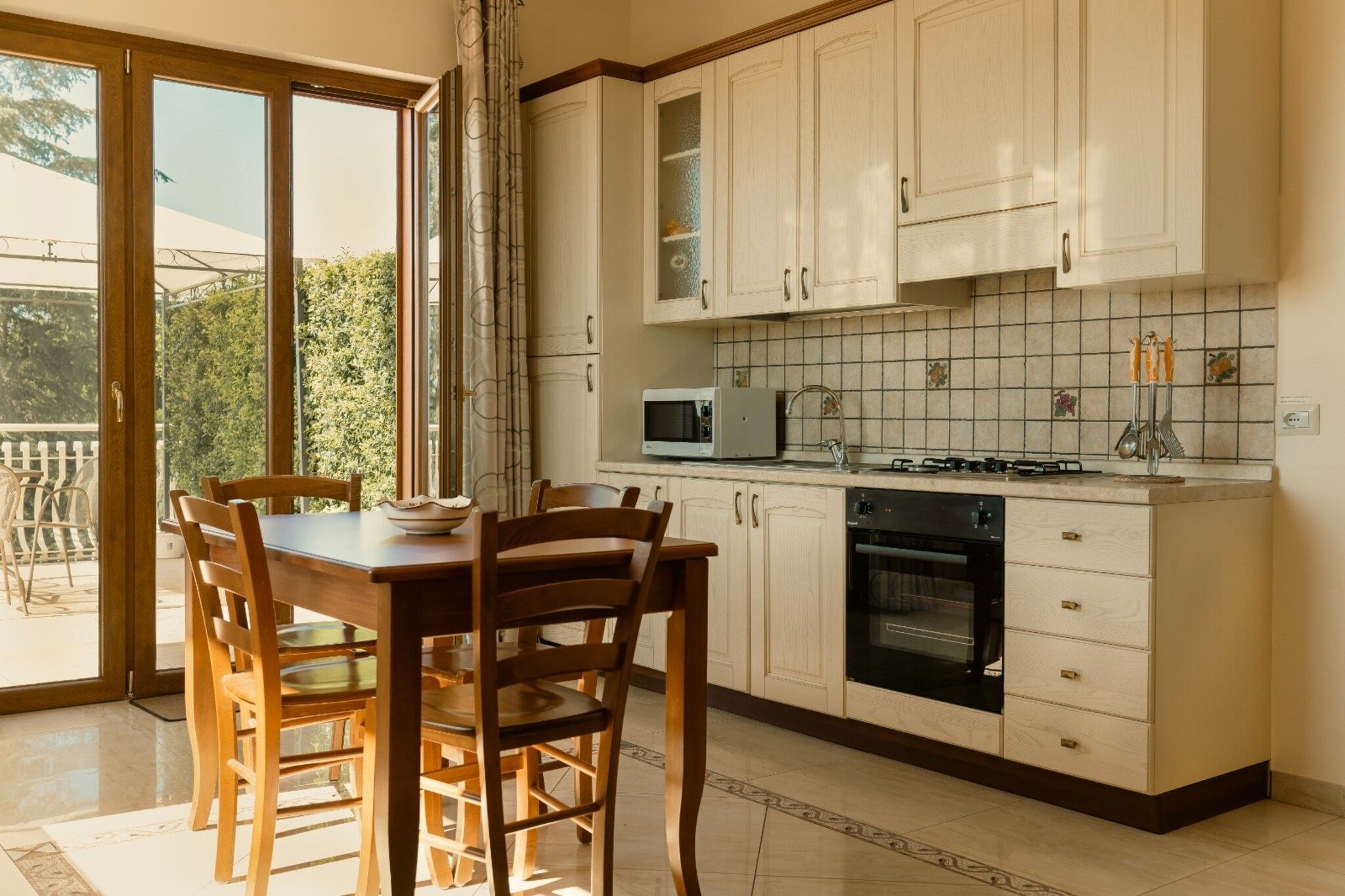 A kitchen with a dining table, chairs, cabinets, a microwave, stove, and a view of greenery outside.