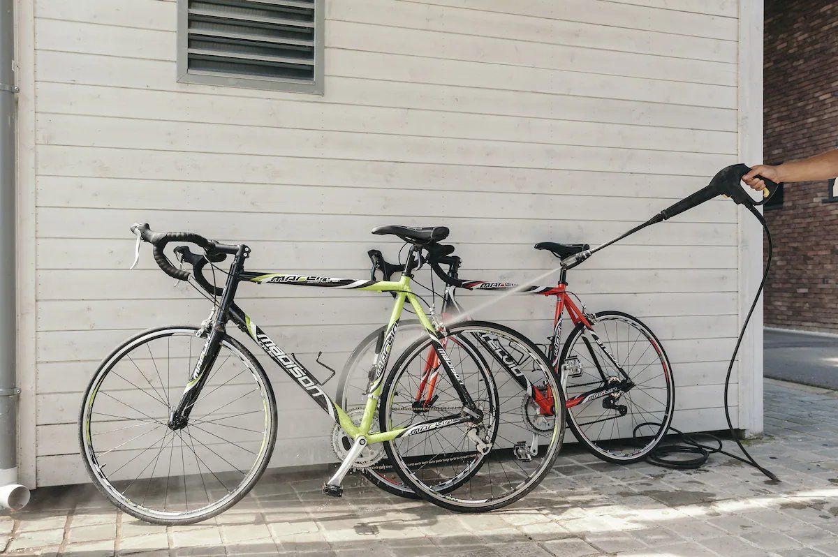 Three bicycles parked against a white building with a window and a brick wall.