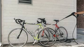 Three bicycles parked against a white building with a window and a brick wall.