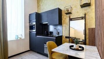 A compact kitchen with dark cabinetry, a built-in oven, and a small dining area with a marble table and a single yellow chair.