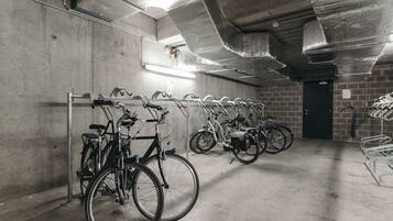 A bike parking area with multiple bicycles parked in rows, a concrete floor, and a door in the background.