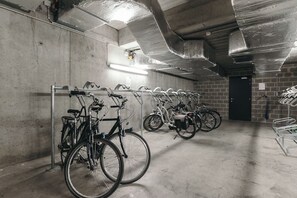 Un espace de stationnement pour vélos où de nombreux vélos sont rangés en rangées, avec un sol en béton et une porte visible au fond.