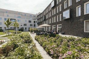 Ein Innenhof mit Sitzgelegenheiten im Freien, ein Garten mit Hortensien und ein modernes Gebäude mit großen Fenstern.
