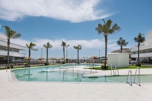 A swimming pool with a tiled deck, surrounded by palm trees and modern buildings. - New 2BR Apt w/ Pool, Terrace & Walk to Beach (Torre del Mar)