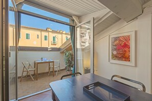 A room with a sliding glass door leading to an outdoor area, a table with chairs, a potted plant, and a framed artwork on the wall. - Apartment 'Corte Regia' with Air Conditioning (Verona)