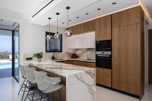 A modern kitchen with marble countertops, wooden cabinets, and stainless steel appliances. - Panoramic Sea View Villa in Hersonissos (Hersonissos)