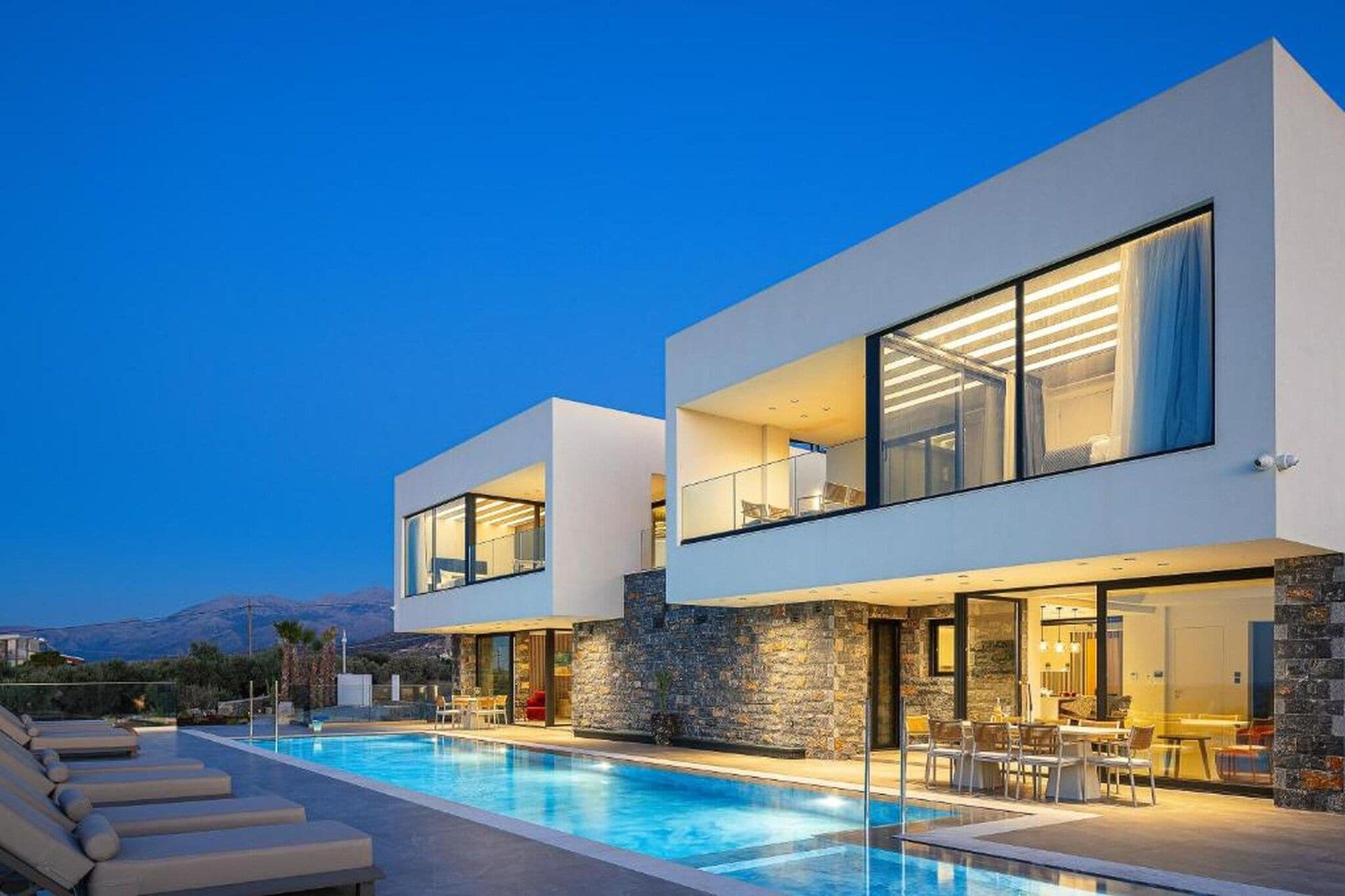 Una casa moderna de dos pisos con piscina, fachada de piedra y ventanas amplias.