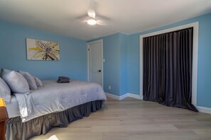 Ein Schlafzimmer mit einem Bett, einem Deckenventilator, einer Tür und einem Fenster mit Vorhängen.