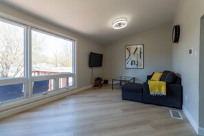 A living room with a large window, a flat-screen TV, a painting, and a sofa with a throw blanket. - Newly Renovated Quiet 2BR | WiFi, Parking & Heat Included—Sleeps up to 6! (London)