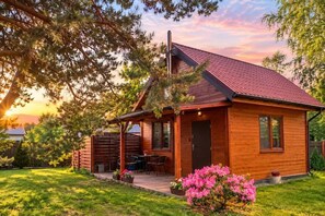 A wooden cabin with a red roof, a porch, and a small garden with pink flowers. - Holiday home for 4 people, Dziwnów (Dziwnów)