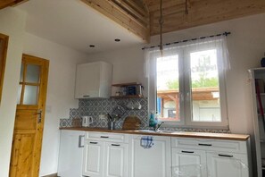 Een keuken met witte kasten, een raam met gordijnen en een houten plafond.