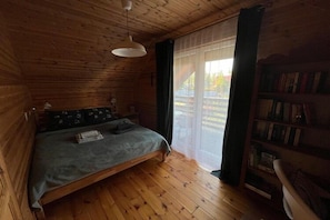 A wooden cabin bedroom with a bed, a bookshelf, and a window. - Holiday home for 6 people Dziwnów (Dziwnów)
