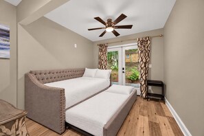 Ein Schlafzimmer mit einem Bett, einem Deckenventilator und Blick durch eine Glastür.