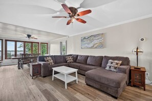Ein geräumiges Wohnzimmer mit einer Eckcouch, einem weißen Couchtisch und einem Deckenventilator.