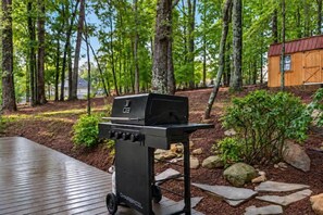 Ein tragbarer Grill auf einer Holzterrasse, im Hintergrund ein Wald.