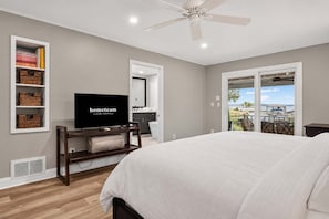 Een slaapkamer met een bed, een televisie, een plafondventilator en uitzicht op de omgeving.