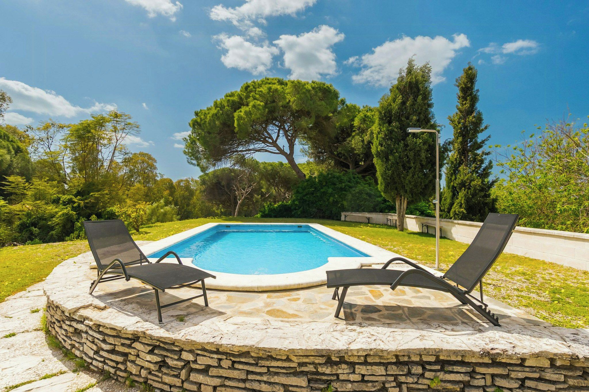 A swimming pool with two lounge chairs and a stone wall surrounding it.