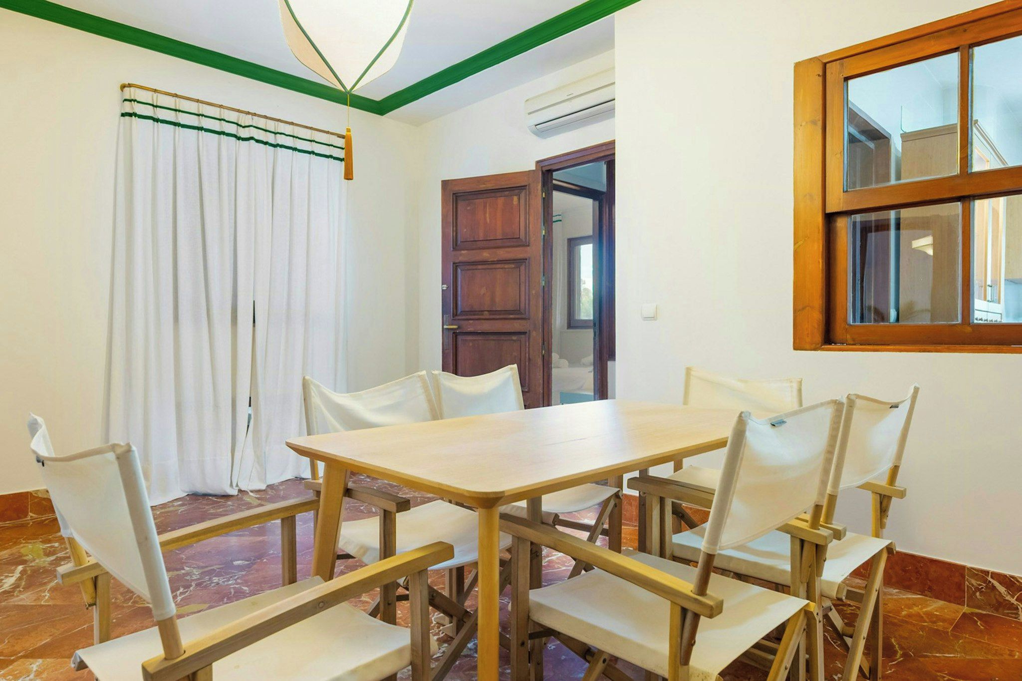 A dining area with a wooden table and chairs, a window with a view, and a door leading to another room.