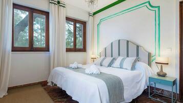 A hotel room with a bed, a nightstand, a lamp, and a view of trees through the window.
