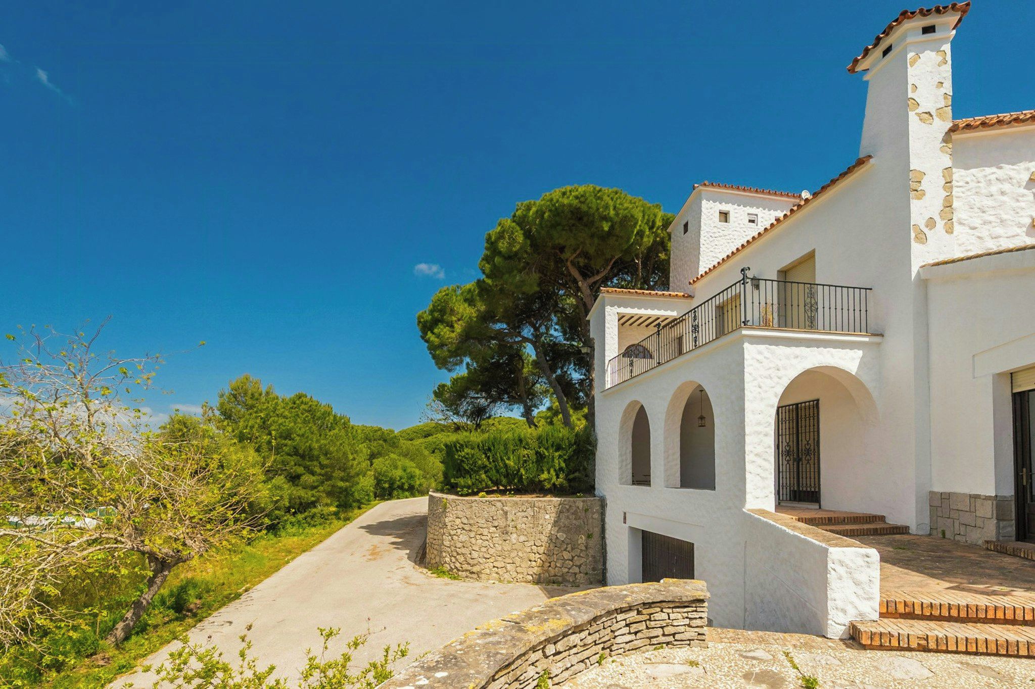 A white building with a balcony, stone walls, and a clear blue sky.