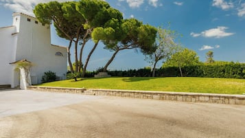 A white building with a stone wall and a grassy area with trees.