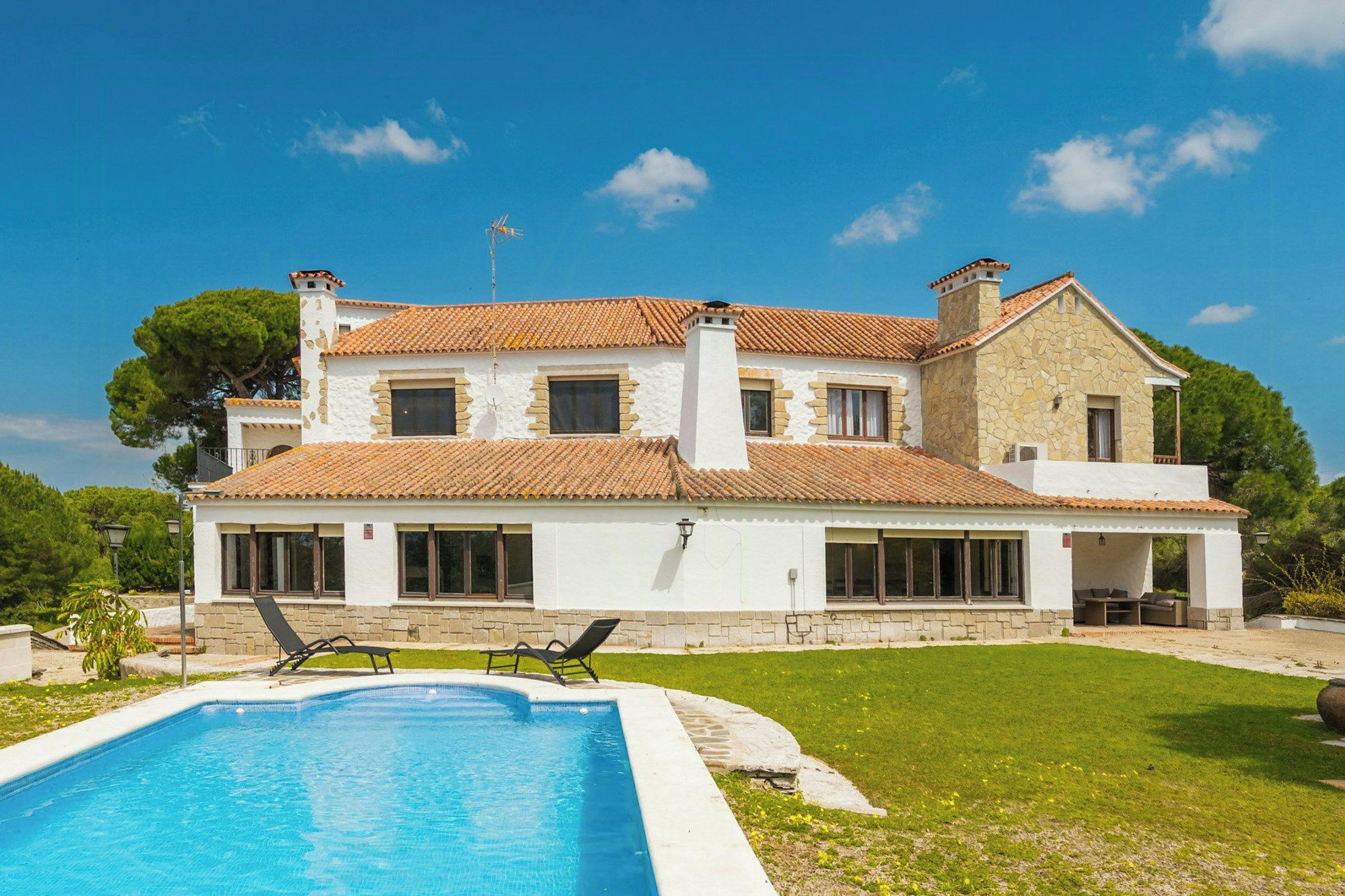 A two-story house with a swimming pool, large windows, and a stone facade.