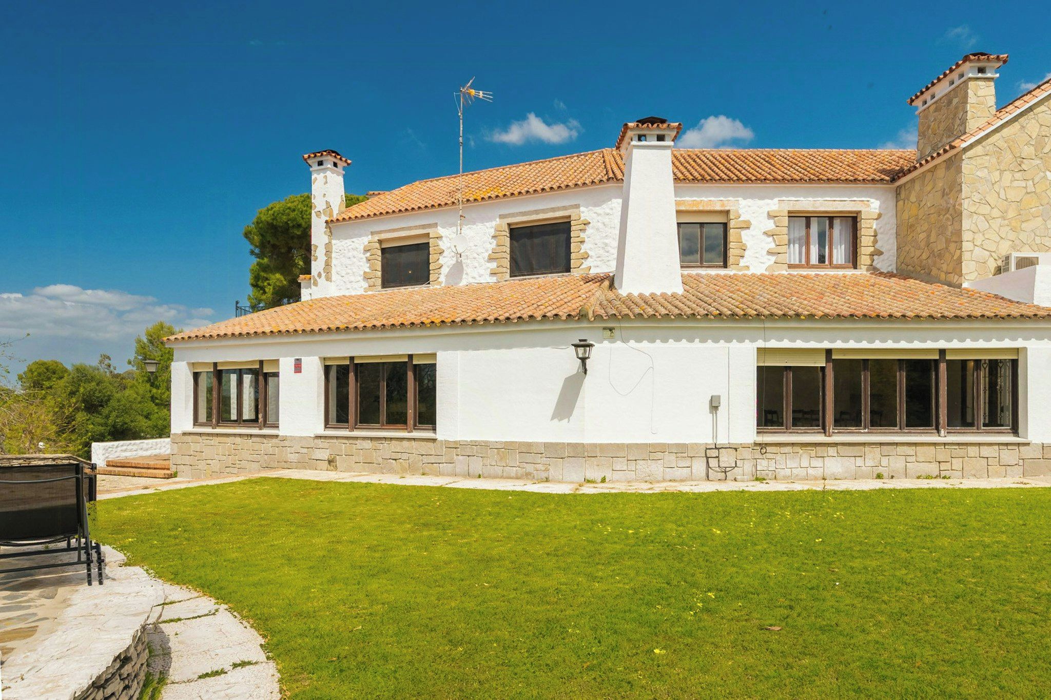 A two-story house with a tiled roof, stone walls, and a well-maintained lawn.