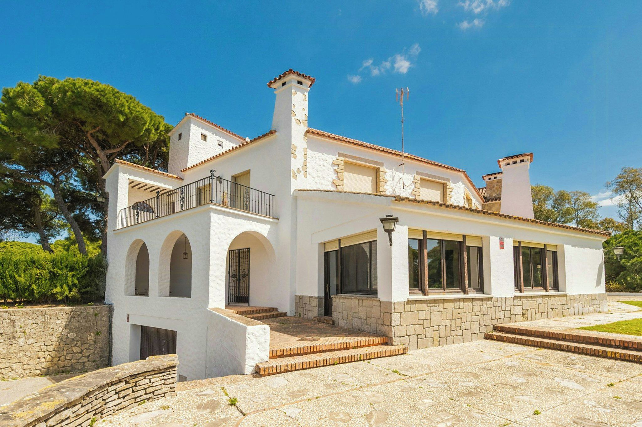 A two-story white building with a balcony, stone steps, and a stone wall.