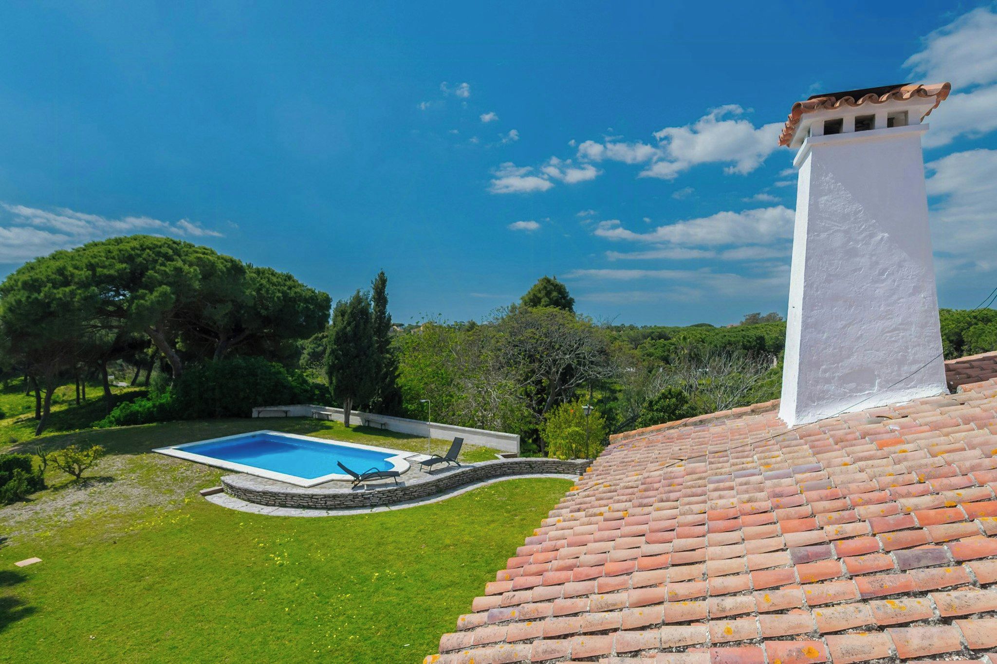 A residential property with a swimming pool, a stone retaining wall, and a tiled roof.