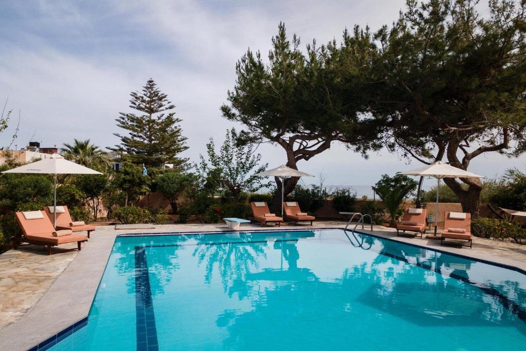 A swimming pool with lounge chairs and umbrellas, surrounded by trees.