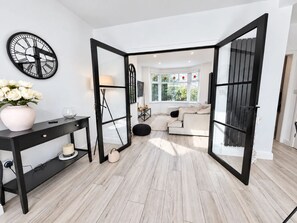A modern living room with a black-framed glass door leading to an adjacent space, a white sofa, and a wall-mounted clock. - Family Home | Free Secure Parking | Pets Allowed - Pass the Keys (Salford)