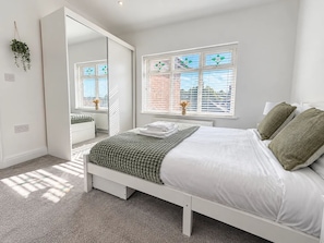 A bedroom with a bed, a window with blinds, a mirror, and a plant. - Family Home | Free Secure Parking | Pets Allowed - Pass the Keys (Salford)